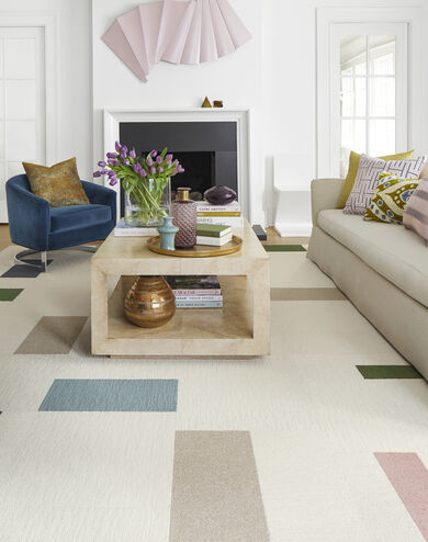 FLOR Made You Look area rug in Bone, Beige, Flannel Blue, Blush, Forest, and Slate, a cream couch, blue chair, and square coffee table.